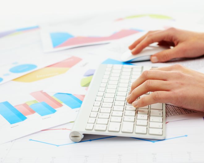 Hände eiern Frau tippen auf einer Tastatur, im Hintergrund liegen Unternehmensdaten in Form von Diagrammen.