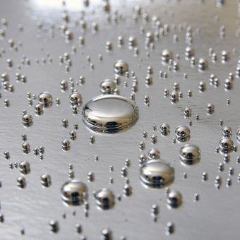Quecksilber: Kleine Tropfen aus flüssigem Quecksilber liegen auf einem silbernen Untergrund