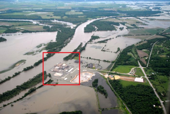 Das Kernkraftwerk Fort Calhoun während der Missouri River Flood am 16. Juni 2011. Wassergefüllte Schlauchbarrieren wurden zum Schutz vor Hochwasser um wichtige Gebäude herum aufgestellt. Weil die Anbindung an das externe Stromnetz zeitweilig vom Hochwasser unterbrochen wurde, musste die Energieversorgung zur Kühlung des Reaktors auf die Notstromdiesel übertragen werden. Rot umrandet sind die Kraftwerksgebäude einschließlich Reaktorgebäude und Maschinenhaus zu sehen.