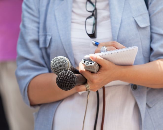 Eine Journalistin hält zwei Mikrophone in der Hand und macht sich auf einem Schreibblock Notizen.