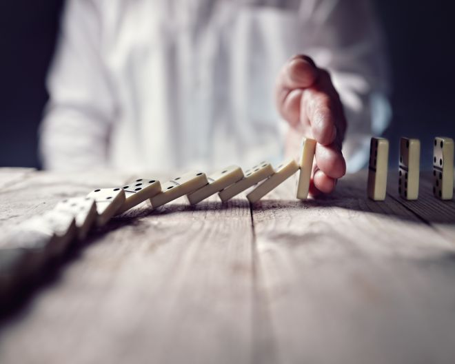 Eine Hand stoppt eine Reihe umfallender Dominosteine