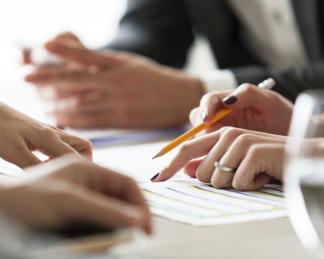 Eine Frauenhand zeigt auf ein Dokument und hält einen Stift in der Hand.