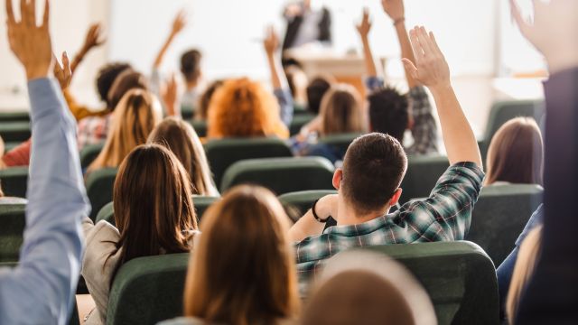 Studierende nehmen an einer Vorlesung teil und geben Handzeichen.