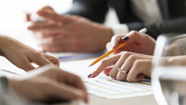 Eine Frauenhand zeigt auf ein Dokument und hält einen Stift in der Hand.