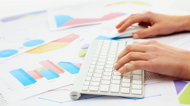 Hände eiern Frau tippen auf einer Tastatur, im Hintergrund liegen Unternehmensdaten in Form von Diagrammen.