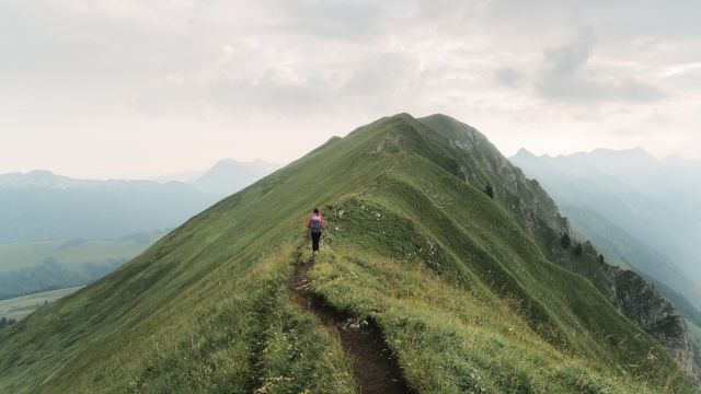 Wanderer geht entlang eines mit Gras bewachsenen Bergrückens
