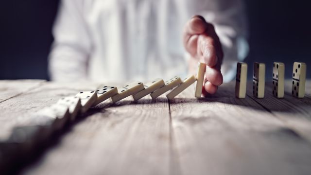 Eine Hand stoppt eine Reihe umfallender Dominosteine