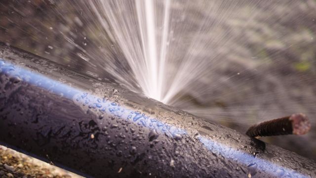 Rohr mit Leck Wasser spritzt aus einem geleckten Rohr
