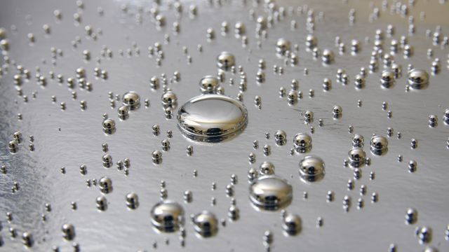 Quecksilber: Kleine Tropfen aus flüssigem Quecksilber liegen auf einem silbernen Untergrund